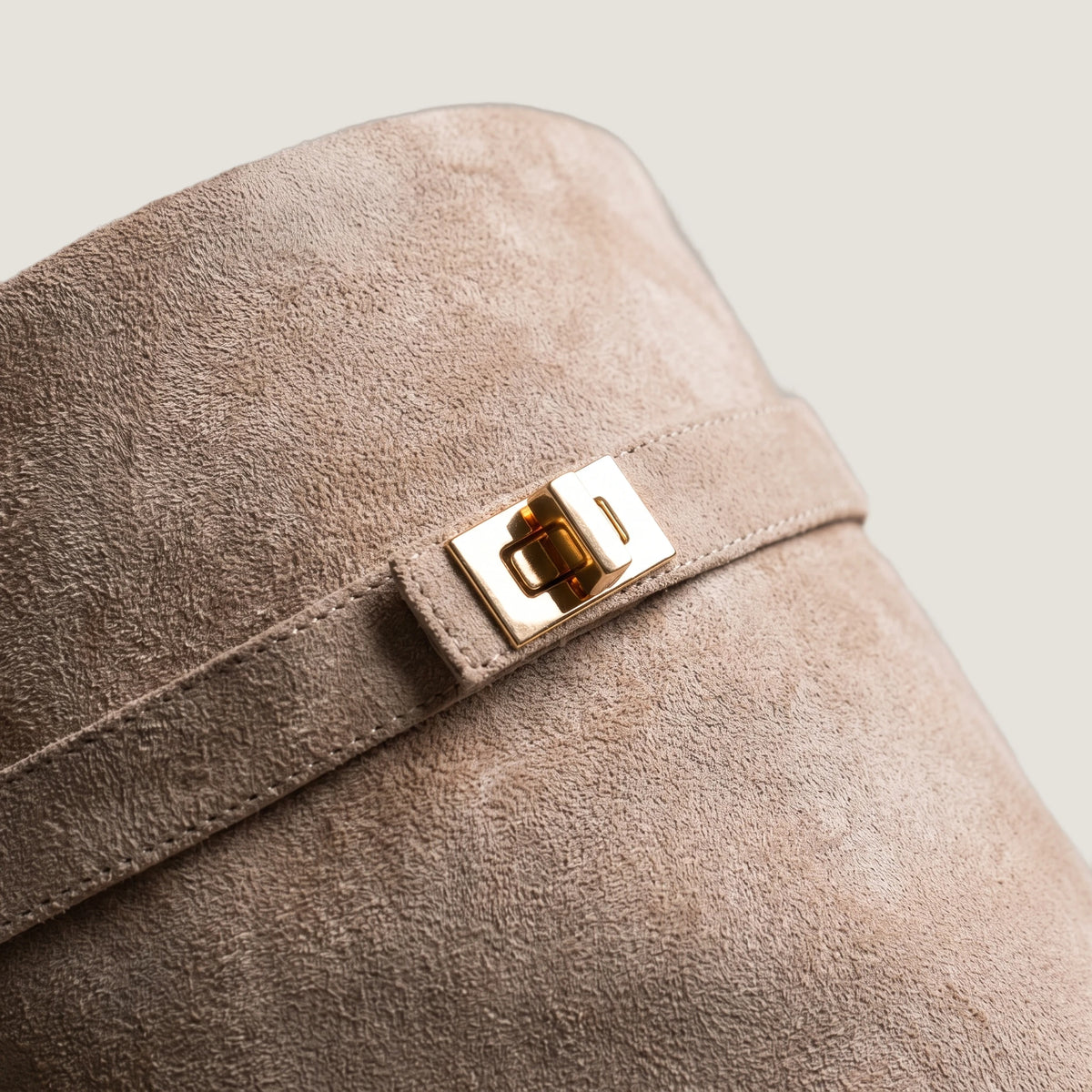 Close-up of the gold turnlock clasp on the beige suede shaft strap