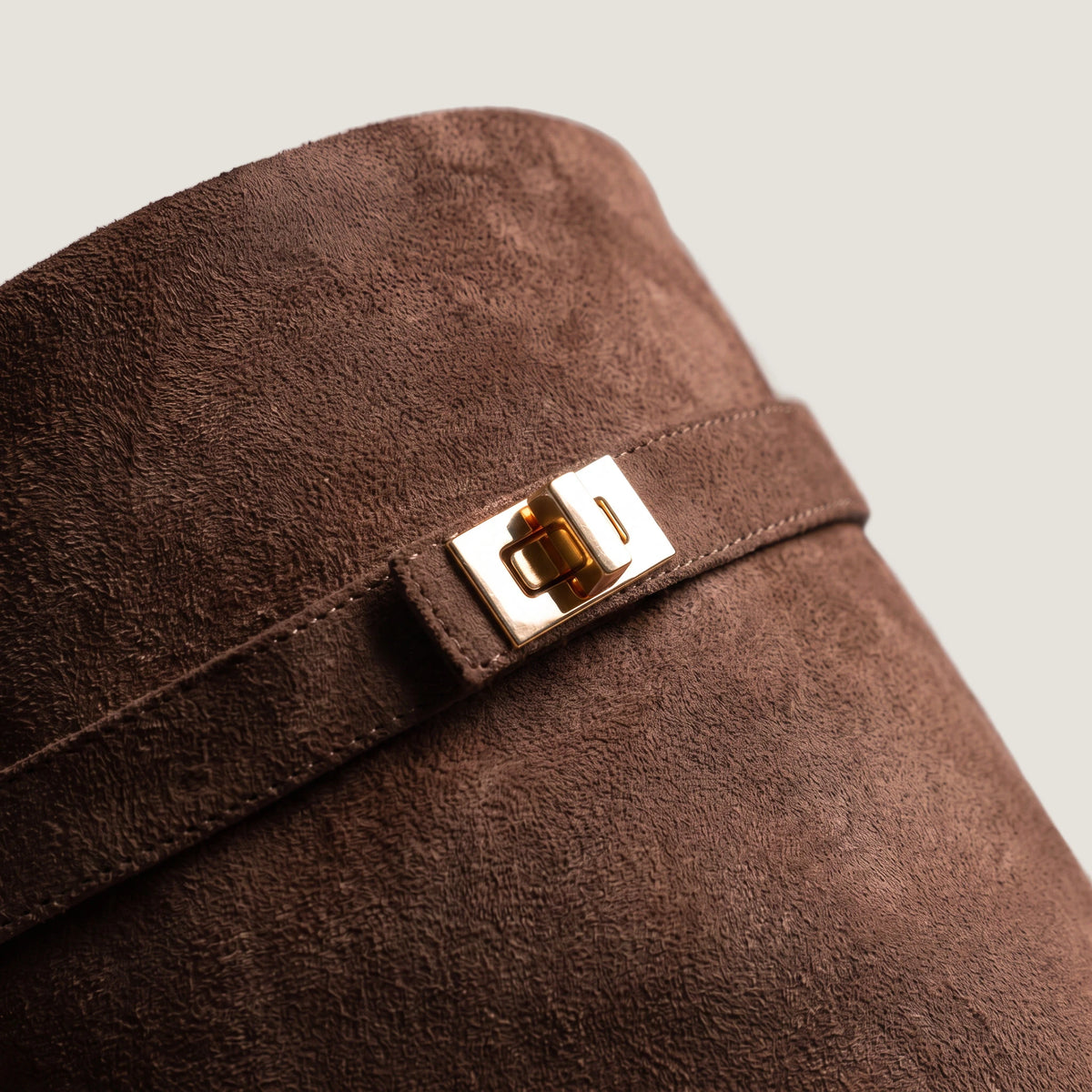 Close-up of the gold turnlock clasp on the dark brown suede shaft strap