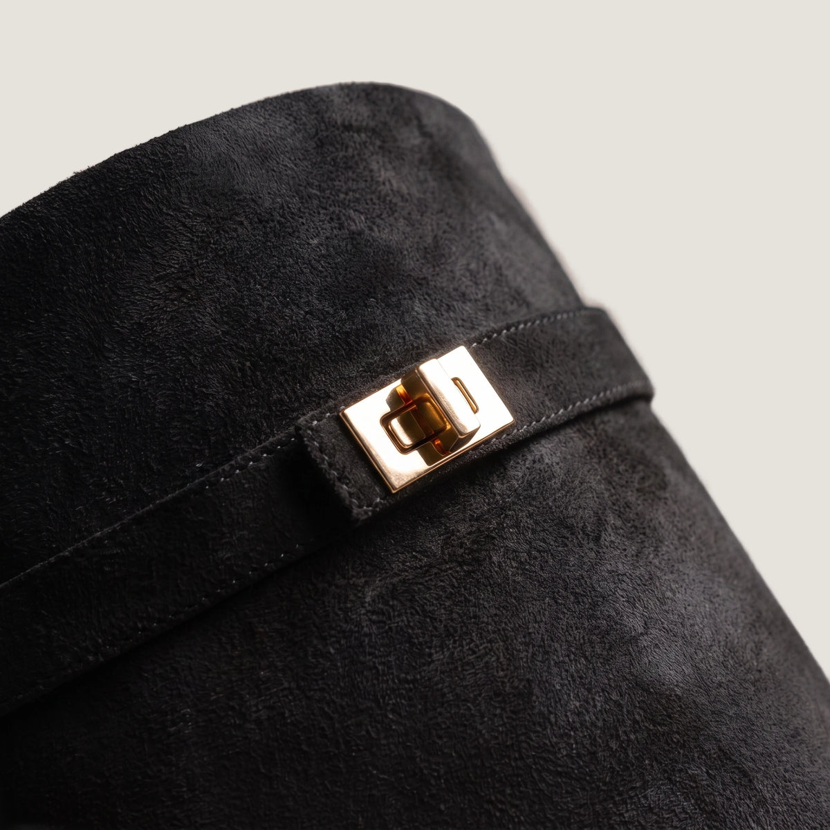 Close-up of the gold turnlock clasp on the black suede shaft strap